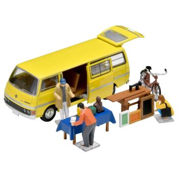 TOM325246 - Rommelmarkt met een gele Nissan Homy bestelbus en accessoires.